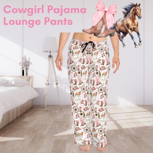 May include: White pajama lounge pants with a repeating pattern of cowboy boots, horses, horseshoes, and wagon wheels. The text "Cowgirl Pajama Lounge Pants" is at the top. The pants have a black drawstring.