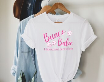 Puede incluir: Camiseta blanca con texto rosa que dice "Bunco Babe I didn't come here to lose" con tres ilustraciones de dados rosas.