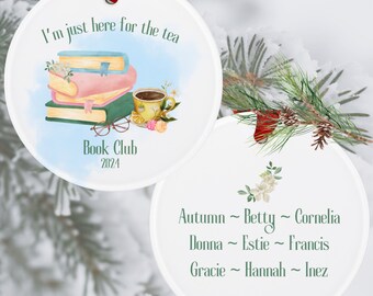 May include: White ceramic ornament with a red ribbon. The front features a watercolor design of books, a teacup, and the text "I'm just here for the tea" and "Book Club 2024." The back lists names.