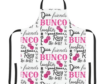 May include: White kitchen apron with a black and pink pattern. The pattern features the words "Dice friends Bunco", "laughter", "good times", "Roll", "Ring the bell!" and dice.