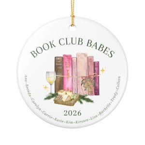 May include: A round white ceramic ornament featuring the text BOOK CLUB BABES at the top and 2026 at the bottom. The center displays a watercolor illustration of five books, a wine glass, cheese, and greenery. Names are listed along the edge.