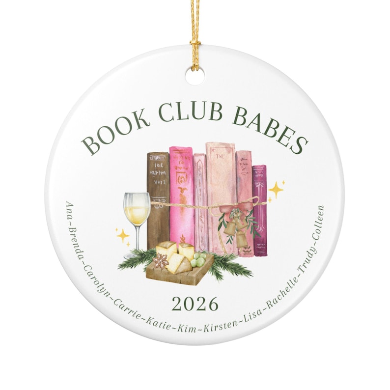 May include: A round white ceramic ornament featuring the text BOOK CLUB BABES at the top and 2026 at the bottom. The center displays a watercolor illustration of five books, a wine glass, cheese, and greenery. Names are listed along the edge.