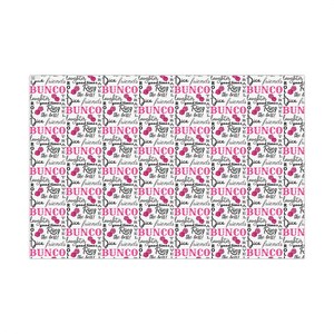May include: Pink and black dice-themed wrapping paper. The design features repeating patterns of dice, the words 'BUNCO', 'ROLL', 'Ring the bell!', 'Dice friends', 'laughter', and 'good times'.  The paper is shown wrapped around several gift boxes.  The text is bold and stylish. The pink dice are a vibrant shade against the white background.