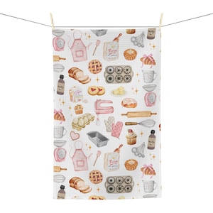 May include: White kitchen towel with a repeating pattern of baking-related illustrations. The design includes images of a pink apron, rolling pin, pie, mixer, measuring cups, and other baking tools and ingredients. The towel is hanging on a clothesline.