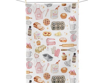 Op de afbeelding: Witte keukendoek met een herhalend patroon van illustraties over bakken. Het ontwerp bevat afbeeldingen van een roze schort, deegroller, taart, mixer, maatbekers en andere bakgereedschappen en ingrediënten. De handdoek hangt aan een waslijn.