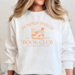 May include: White long-sleeved sweatshirt with an orange graphic design that says "Pumpkin Patch Book Club Est. 2024 Invitation Only" with a drawing of pumpkins and a house.