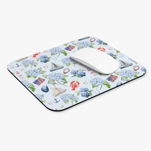 May include: A rectangular mouse pad with a light blue background featuring a repeating pattern of blue hydrangea flowers, sailboats, American flags, red lobsters, seashells, and anchors, with a white computer mouse resting on top.