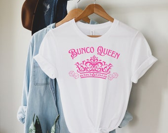 May include: White t-shirt with pink text that reads "Bunco Queen" and a pink crown with dice on either side.