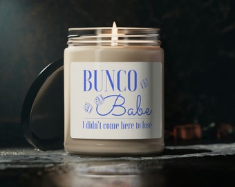 May include: A brown glass candle with a white label that reads "BUNCO Babe I didn't come here to lose". The label also features blue dice graphics.
