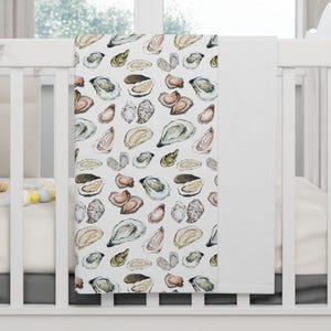May include: A white baby blanket with a pattern of watercolor oysters in shades of brown, gray, and green.