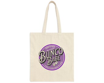 Op de afbeelding: Crèmekleurige draagtas met een paarse en witte cirkelvormige afbeelding. De afbeelding leest "Certified Award Winning Bunco Babe" met dobbelstenen en de zin "I didn't come here to lose."