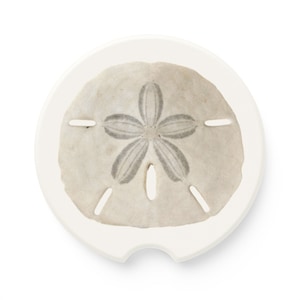 May include: A white ceramic coaster with a sand dollar design. The sand dollar is beige with a gray five-pointed star in the center.
