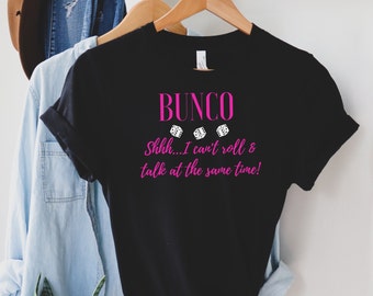 Puede incluir: Camiseta negra con texto rosa que dice "BUNC0 Shhh... I can't roll & talk at the same time!" con tres imágenes de dados blancos.
