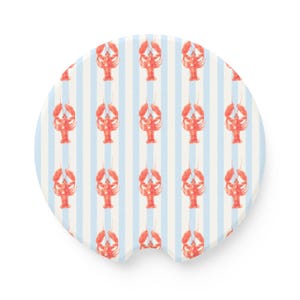 May include: A round car coaster featuring a pattern of red lobsters on a background of alternating light blue and white vertical stripes. The coaster has a small notch on one side.