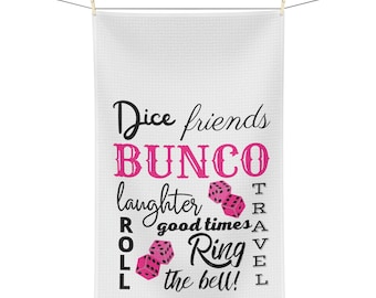 Peut inclure: Serviette de cuisine blanche avec du texte noir qui dit "Dice friends BUNCO laughter good times ROLL Ring the bell!" avec des illustrations de dés roses.