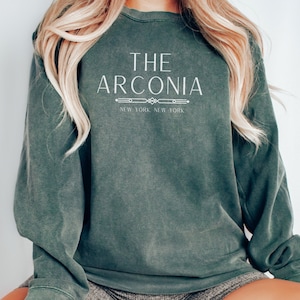Pode incluir: Uma camisa de moletom verde escura com o texto "THE ARCONIA NEW YORK NEW YORK" impresso em branco.