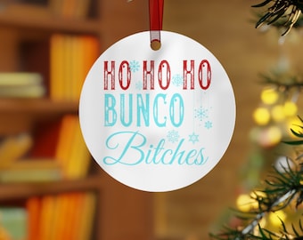 May include: White round Christmas ornament with the text "Ho Ho Ho Bunco Bitches" in red and blue lettering with snowflake designs.