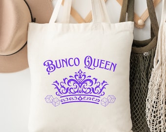 Op de afbeelding: Een witte canvas tote bag met paarse tekst die "BUNC0 QUEEN" zegt en een paarse kroon met dobbelstenen aan beide kanten.