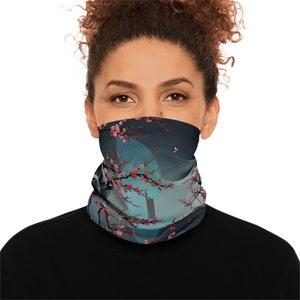 Pode incluir: Uma máscara facial com fundo azul e cinza apresentando um ramo de cerejeira estilizado com flores cor-de-rosa e uma borboleta. A máscara é feita de um tecido macio e respirável.