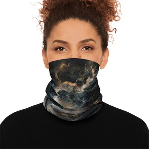 Può includere: Un scaldacollo nero e oro con un design a nebulosa. Lo scaldacollo è realizzato in un materiale morbido ed elastico e può essere indossato come copertura per il viso o come scaldacollo. Il design presenta accenti dorati e bianchi.