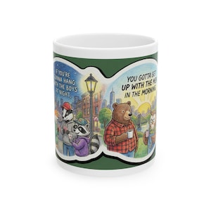 May include: White ceramic mug with a green border featuring cartoon illustrations of animals in a city setting. One side shows a badger, raccoon, and text "IF YOU'RE GONNA HANG WITH THE BOYS AT NIGHT." The other side shows a bear, owl, and text "YOU GOTTA GET UP WITH THE MEN IN THE MORNING."