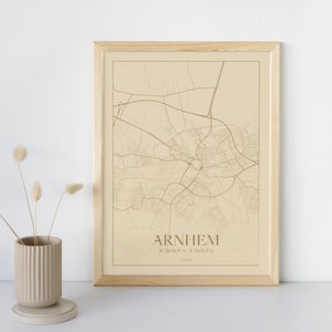 Op de afbeelding: Een ingelijste kaartprint van Arnhem, Nederland, met een beige achtergrond en bruine lijnen die de straten van de stad weergeven. De naam van de stad "Arnhem" is onderaan de kaart in bruin gedrukt, samen met de coördinaten "51.9869° N, 5.5417° E".