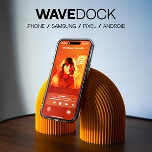 May include: An orange phone stand with a clear phone case holding a phone displaying a music app. The stand is supporting a phone and has the text "WAVEDOCK" at the top. The phone is charging and the screen displays the song "De Imperto".