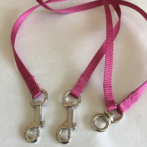 Op de afbeelding: Drie roze hondenriemen met zilveren metalen clips. De riemen zijn gemaakt van geweven nylon.