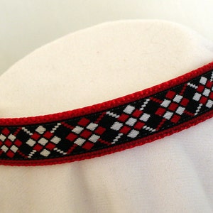 Puede incluir: Un collar de perro rojo, negro y blanco con una hebilla plateada.