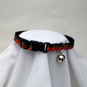May include: Black cat collar with a red and yellow flame pattern and a silver bell.