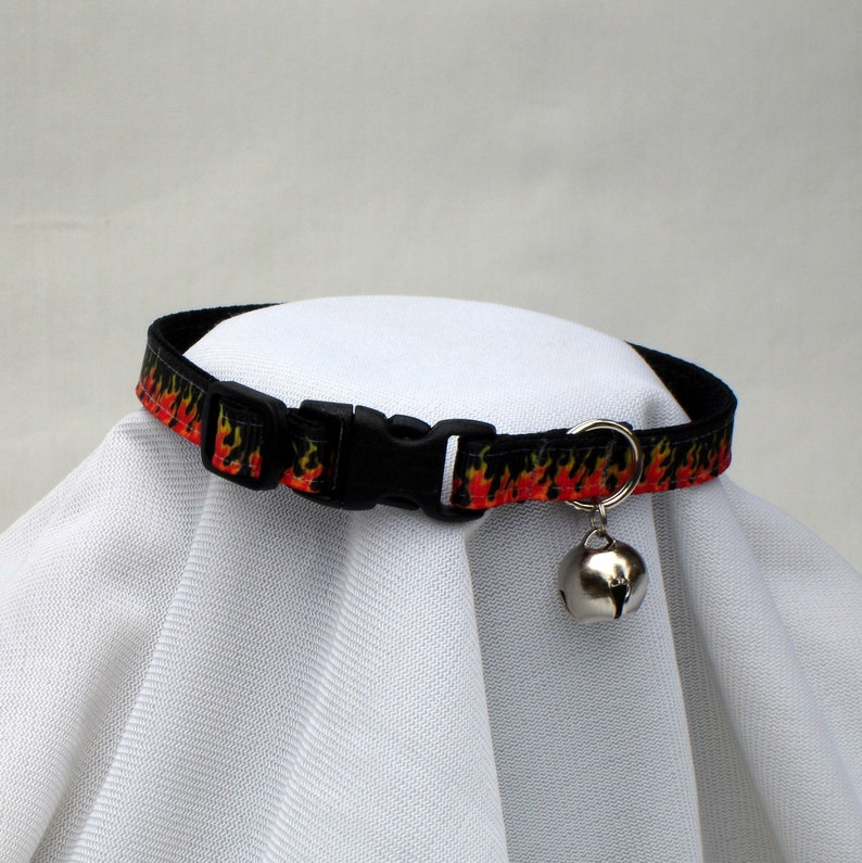May include: Black cat collar with a red and yellow flame pattern and a silver bell.