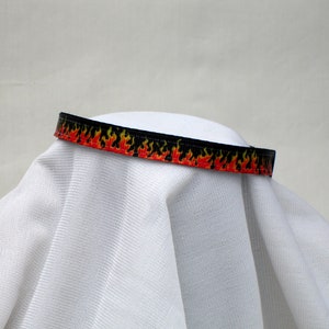 May include: A black and red ribbon with a flame pattern. The ribbon is on a white surface.