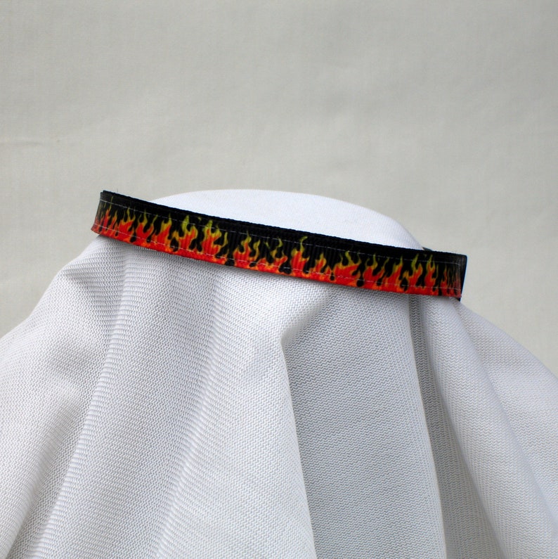 May include: A black and red ribbon with a flame pattern. The ribbon is on a white surface.