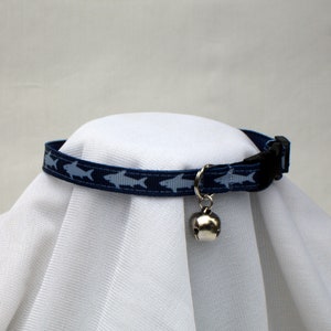 May include: A blue cat collar with a white shark pattern and a silver bell.