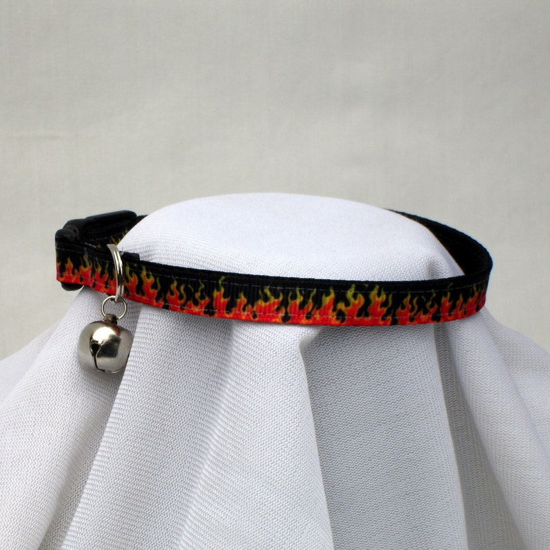 May include: A black cat collar with a red and yellow flame pattern and a silver bell.