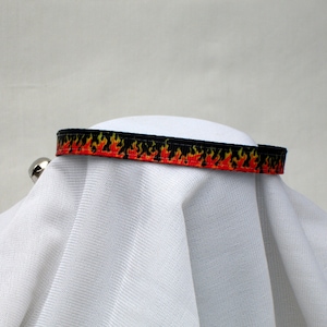 May include: A black and orange ribbon with a flame pattern. The ribbon is on a white surface.
