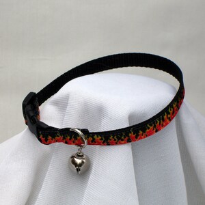 May include: Black cat collar with a red and yellow flame pattern and a silver bell.