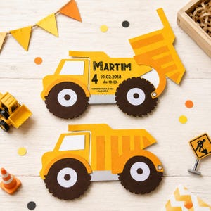 May include: Two yellow and brown construction truck-shaped invitations with the name "Martim" and event details. The invitations are surrounded by construction-themed decorations, including a toy bulldozer, a traffic cone, and a road work sign.