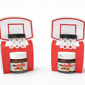 May include: Two miniature basketball hoops with red backboards and white nets. Each hoop has a small jar of Nutella at the base. The jars have white lids and brown labels with the Nutella logo.