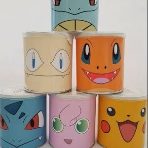 Puede incluir: Una colección de siete recipientes cilíndricos, cada uno adornado con una cara de personaje de dibujos animados diferente. Los recipientes presentan una variedad de colores, incluyendo azul, naranja, amarillo y rosa, con tapas blancas. Las caras son expresivas y detalladas.