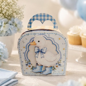 May include: A light blue gift box with a white duck illustration wearing a blue bow tie and boots. The box has a gingham handle and floral accents. The overall design is soft and whimsical, suitable for a baby shower or similar event.