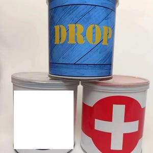 May include: Three round metal containers with lids. The top container is blue with white wood grain and the word "DROP" in yellow letters. The middle container is white with a blue circle and the bottom container is white with a red circle and a white plus sign.