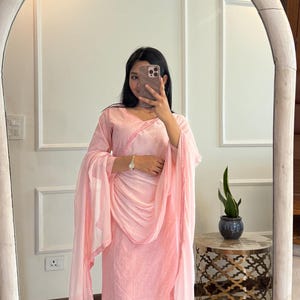 May include: A light pink salwar kameez set, including a tunic, pants, and a dupatta. The tunic and dupatta have delicate pink trim. The outfit is made of a lightweight fabric. The person in the image is wearing silver sandals.