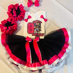 May include: A white t-shirt with a graphic that says "Happy Birthday Asa" and the number 8, paired with a black tutu skirt with pink and white trim. The set includes pink hair bows and scrunchies. A birthday outfit.