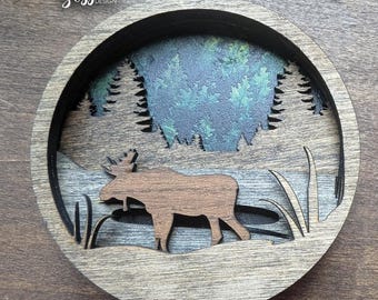 Adorno navideño de alce en capas SVG, archivo cortado con láser con pinos y lago