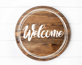 May include: Round wooden sign with a white painted welcome message and a white painted circle border.