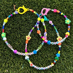 May include: Multicolored beaded necklaces with charms, including flowers, stars, and the words "Cool Cat" and "Jake Jake".