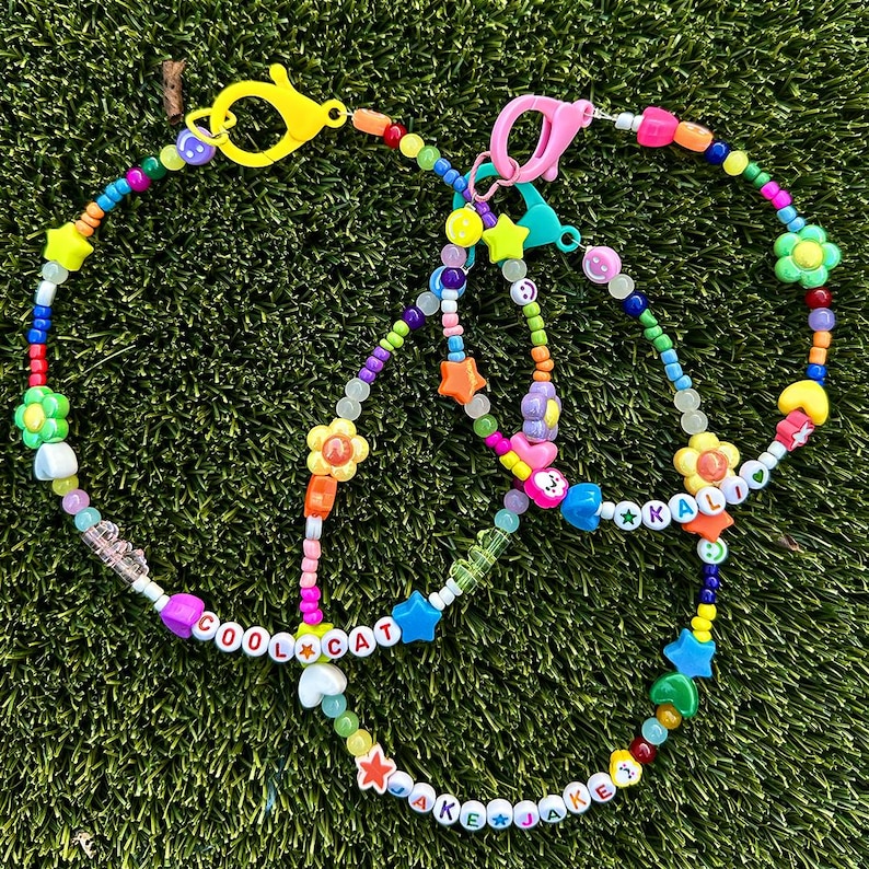 May include: Multicolored beaded necklaces with charms, including flowers, stars, and the words "Cool Cat" and "Jake Jake".