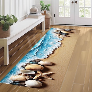 Puede incluir: Una alfombra rectangular con una escena de playa con un océano azul, arena color arena, conchas marinas y una estrella de mar. El diseño de la alfombra incluye detalles realistas de olas, guijarros y varias conchas marinas, creando un tema costero.