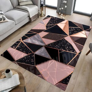 Pode incluir: Tapete com padrão geométrico com um design moderno. O tapete apresenta uma mistura de tons preto, rosa, cinza e bronze dispostos em um padrão triangular. O tapete está colocado em um piso de madeira.